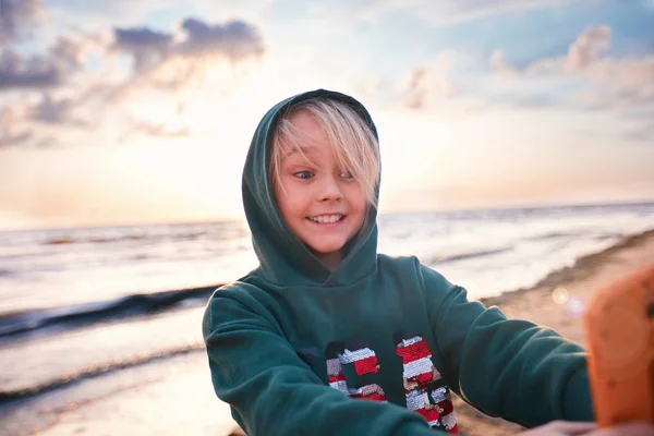 Bonito menino feliz fazendo selfie no telefone no por do sol, na praia — Fotografia de Stock