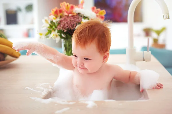 Schattige kleine baby meisje het nemen van een bubbelbad in een keuken gootsteen — Stockfoto