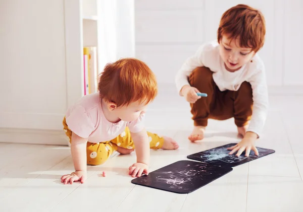 Cute redhead siblings having fun, drawing on chalk board at home — Stock Photo, Image