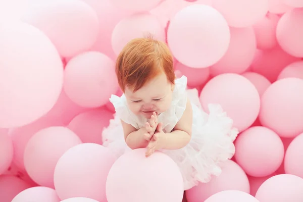 Adorable, little baby girl is delighted by standing among pastel pink balloons on the party — Stock Photo, Image