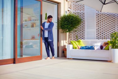 Aile yazın verandada dinlenirken, adam sürgülü kapıları açar.