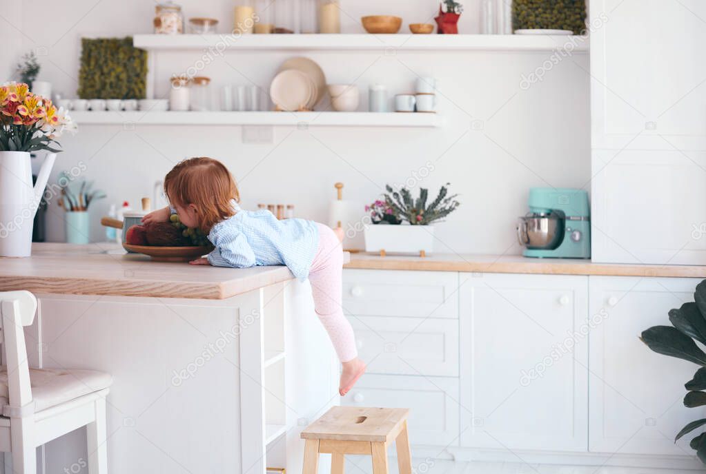 curious infant baby girl trying to reach the fruit on the table in the kitchen with the help of step stool