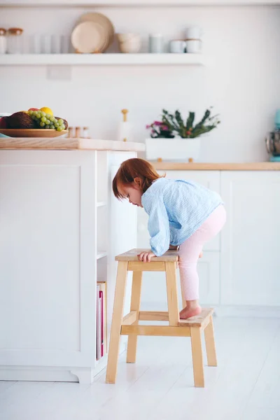 面白い赤ちゃんの女の子は家の居心地の良いキッチンでステップスツールを登る — ストック写真