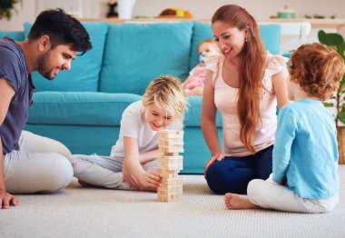 Neşeli aile eğleniyor, evdeki halıda ahşap blok oyunu oynuyorlar.