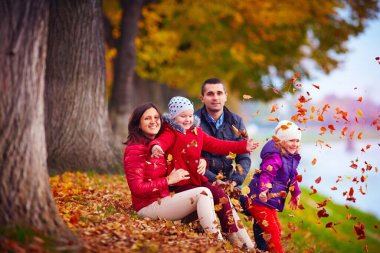 Sonbahar parkında düşen yaprakların arasında oynayan mutlu bir aile.
