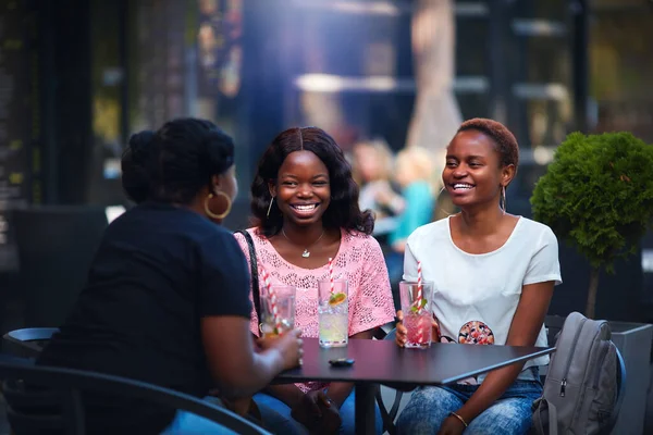 Happy African American Women, friends sitting together at the outdoor restaurant at summer day