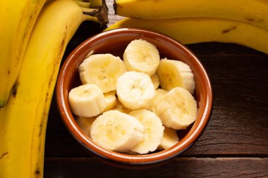 Bir demet muz ve dilimlenmiş muz bir tencerede ahşap bir masanın üzerinde..