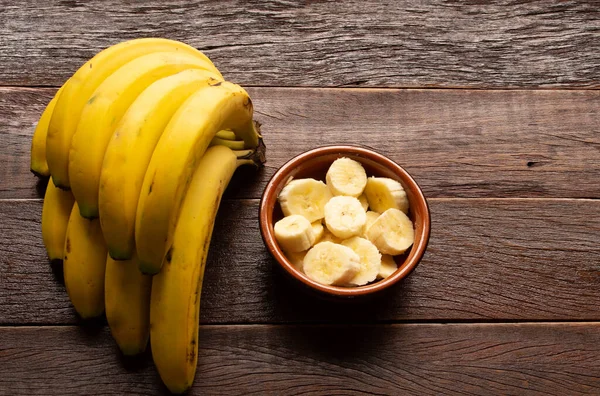 A bunch of bananas and a sliced banana in a pot over a wooden table.