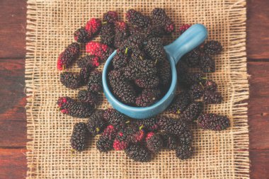 Taze böğürtlenler ahşap masada mavi bir kasede kırsal bir kenevirle