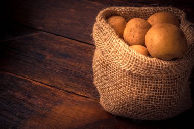 Taze ve çiğ patatesler ahşap masadaki kırsal bir çuvalda.