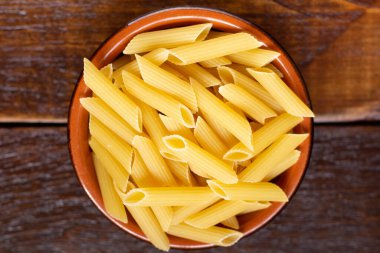 Tam yağlı makarna. Kahverengi bir kâseye konan İntegral Penne ahşap bir masanın üzerinde tahta bir kaşık gibidir.