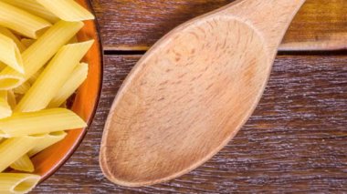 Tam yağlı makarna. İntegral Penne kahverengi bir kâseye, tahta bir kaşıkla ahşap bir masanın üstüne konuyor.