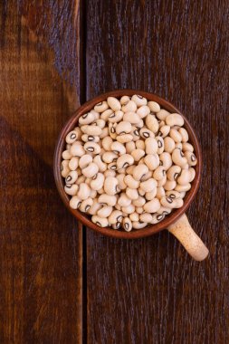 Many grains of brown raw beans in cup on wooden table 