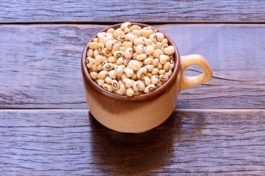 Many grains of brown raw beans in cup on wooden table 