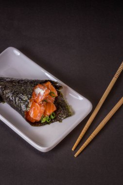 Siyah arka planda beyaz tabakta somon temaki suşisi.