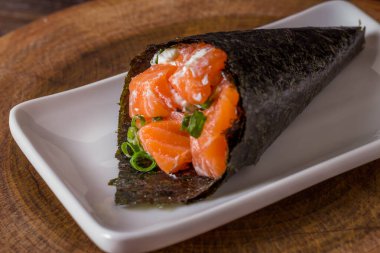 Siyah arka planda beyaz tabakta somon temaki suşisi.