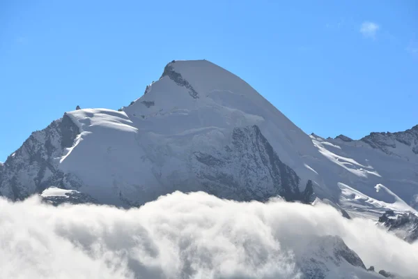 艾拉林洪峰的顶峰在云彩之上升起 右边是瑞士阿尔卑斯山Saas Fee上方Mittel Allalin的旋转冰川餐厅 — 图库照片