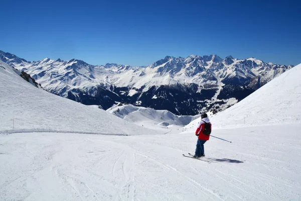 在阳光灿烂的天气里 一个人在广袤的露天滑雪场上滑雪 背靠着高山 — 图库照片