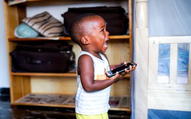 Kampala, Uganda - 01 Temmuz 2017: Küçük Afrikalı çocuk ağlıyor çünkü annesi uzun süre telefon oyunu oynamasına izin vermiyor, küçük çocukların öfke nöbeti, alet bağımlılığı olan şımarık bir çocuk.