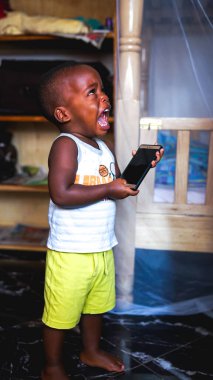 Kampala, Uganda - 01 Temmuz 2017: Küçük Afrikalı çocuk ağlıyor çünkü annesi uzun süre telefon oyunu oynamasına izin vermiyor, küçük çocukların öfke nöbeti, alet bağımlılığı olan şımarık bir çocuk.