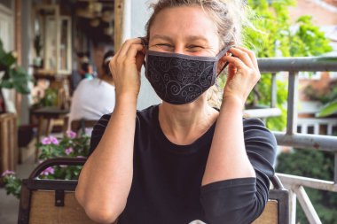 Yeni normal moda, çok mutlu beyaz bir kız siyah tıbbi koruma maskesi takıyor, virüs ve kirlilik güvenlik önlemleri, sosyal mesafeler ve covid 19 yayılmasını engelliyor.