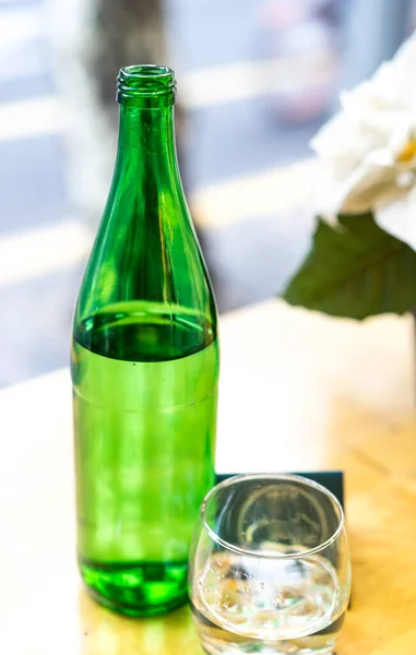 Mineral water in a green glass bottle with a glass on the wooden table at the restaurant, welcome drink, selective focus, beautiful blurred bokeh, green bottle of water. Bottle and a glass