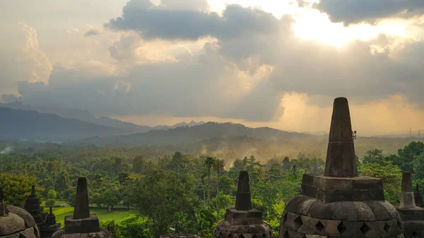 インドネシアの東ジャワのボロブドゥール寺院での栄光の夕日 丘の上の青とオレンジの空 緑のジャングルと仏塔 旅行先 ユネスコ世界遺産 — ストック写真