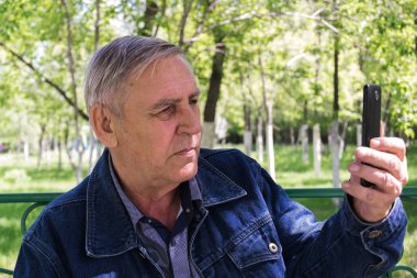 Parkta telefonu olan yaşlı adam.