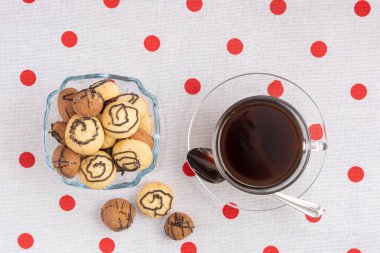 Kurabiyeli vazo ve bir fincan kahve. Bir tabak tabak üzerinde bir cam bardak duruyor. Bir çay kaşığının yakınında.