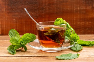 Cam bardakta naneli çay. Bir fincan ve bir masaya nane yaprakları.