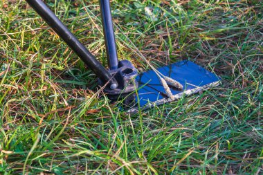 Bozuk bir akıllı telefon çimlerin üzerinde yatıyor. Dokunma ekranı kırılmış. Katlanan sandalyenin bacağı ekranda duruyor..