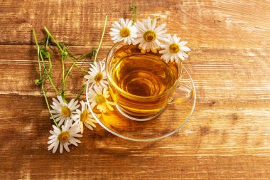 Tahta bir arka planda cam bir fincanda papatya çayı..