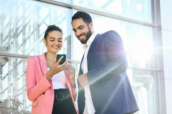 Welcome on board! Two handsome men shaking hands with smile while sitting on the couch at office with their coworkers