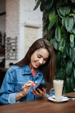 Genç bir kadın kafede mesajlaşıyor ya da akıllı telefon kullanıyor ve kahve içiyor. Şehir yaşam tarzı, kafe yaşam tarzı, modern hayat..