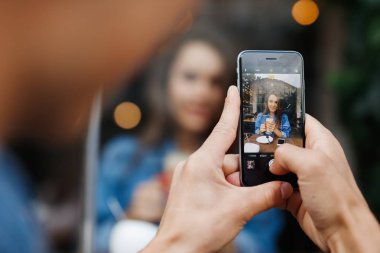 Oğlan telefonda kafedeki pencereden bir kız fotoğrafı çekiyor.