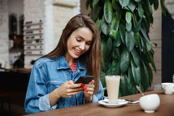 Genç bir kadın kafede mesajlaşıyor ya da akıllı telefon kullanıyor ve kahve içiyor. Şehir yaşam tarzı, kafe yaşam tarzı, modern hayat..