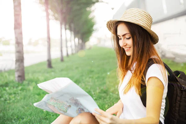 Young smiling  traveler girl searching location on map sitting on bench. during a summer trave