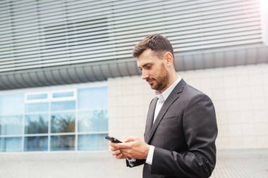 Bir smartphone kullanarak yakışıklı bir iş adamı. Uzaktan çalışma kavramında akıllı telefon kullanarak çalışma. İş ve bilgi teknolojisi kavramı. şehir içinde belgili tanımlık geçmiş ile ayakta sokak