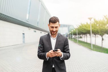 Bir smartphone kullanarak yakışıklı bir iş adamı. Uzaktan çalışma kavramında akıllı telefon kullanarak çalışma. İş ve bilgi teknolojisi kavramı. şehir içinde belgili tanımlık geçmiş ile ayakta sokak