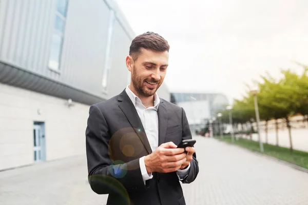 Bir smartphone kullanarak yakışıklı bir iş adamı. Uzaktan çalışma kavramında akıllı telefon kullanarak çalışma. İş ve bilgi teknolojisi kavramı. şehir içinde belgili tanımlık geçmiş ile ayakta sokak