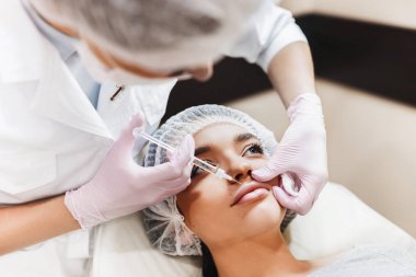 Dudak geliştirme süreci. Makyajcısı hyaluronik asit enjeksiyonu bir güzel dudaklarında yapar. Çok güzel bir yüzün özel şapka ve bir doktor pembe eldiven eller genç kızla.
