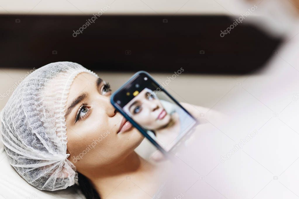 The doctor makes a photo of the lips before enhancement in order to see the difference. The young girl with a beautiful face in a special face.
