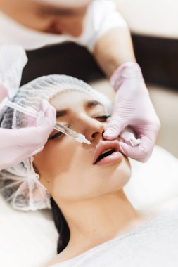 Dudak geliştirme süreci. Makyajcısı hyaluronik asit enjeksiyonu bir güzel dudaklarında yapar. Çok güzel bir yüzün özel şapka ve bir doktor pembe eldiven eller genç kızla.