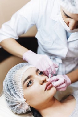 Dudak geliştirme süreci. Makyajcısı hyaluronik asit enjeksiyonu bir güzel dudaklarında yapar. Çok güzel bir yüzün özel şapka ve bir doktor pembe eldiven eller genç kızla.