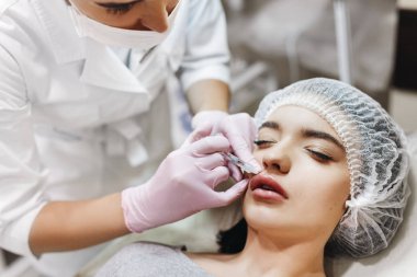 Dudak geliştirme süreci. Makyajcısı hyaluronik asit enjeksiyonu bir güzel dudaklarında yapar. Çok güzel bir yüzün özel şapka ve bir doktor pembe eldiven eller genç kızla.