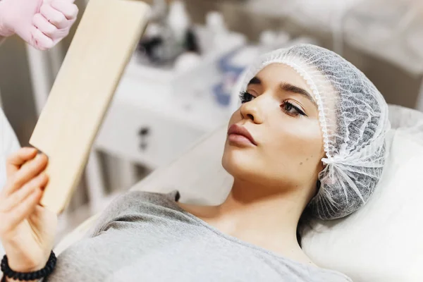 Dudak geliştirme için hazırlık süreci. Doktor hastanın önünde hyaluronik asit yukarı çekiyor. Çok güzel bir yüzün özel şapka ve bir doktor pembe eldiven eller genç kızla