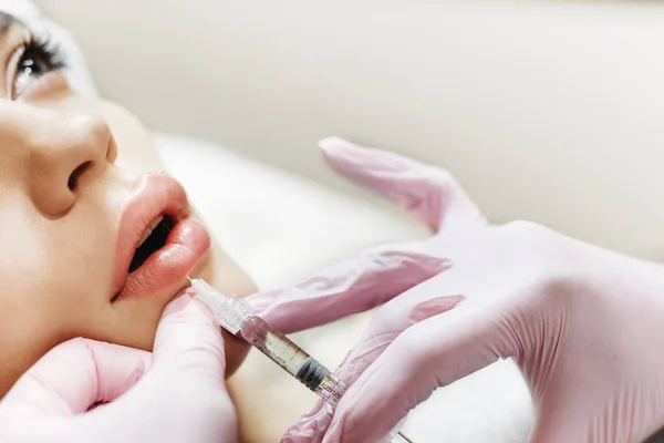 Dudak geliştirme süreci. Makyajcısı hyaluronik asit enjeksiyonu bir güzel dudaklarında yapar. Çok güzel bir yüzün özel şapka ve bir doktor pembe eldiven eller genç kızla.