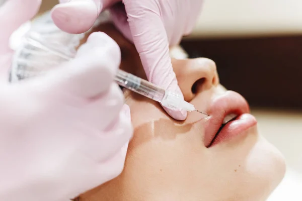 Dudak geliştirme süreci. Makyajcısı hyaluronik asit enjeksiyonu bir güzel dudaklarında yapar. Çok güzel bir yüzün özel şapka ve bir doktor pembe eldiven eller genç kızla.