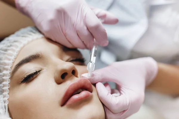 Dudak geliştirme süreci. Makyajcısı hyaluronik asit enjeksiyonu bir güzel dudaklarında yapar. Çok güzel bir yüzün özel şapka ve bir doktor pembe eldiven eller genç kızla.