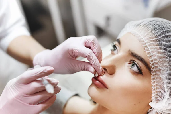 Dudak geliştirme için hazırlık süreci. Doktor hastanın önünde hyaluronik asit yukarı çekiyor. Çok güzel bir yüzün özel şapka ve bir doktor pembe eldiven eller genç kızla